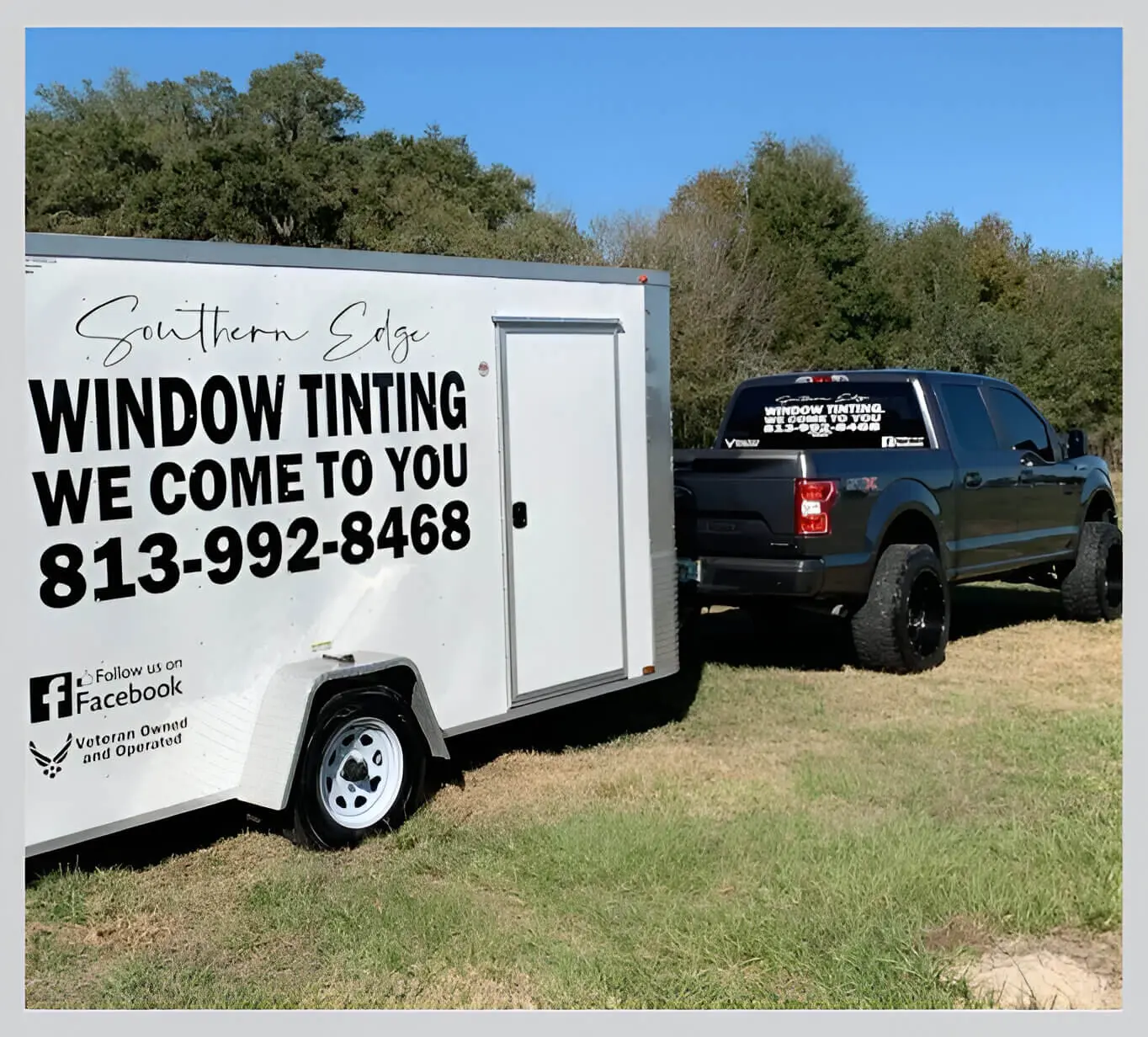 A truck parked in the grass next to a trailer.