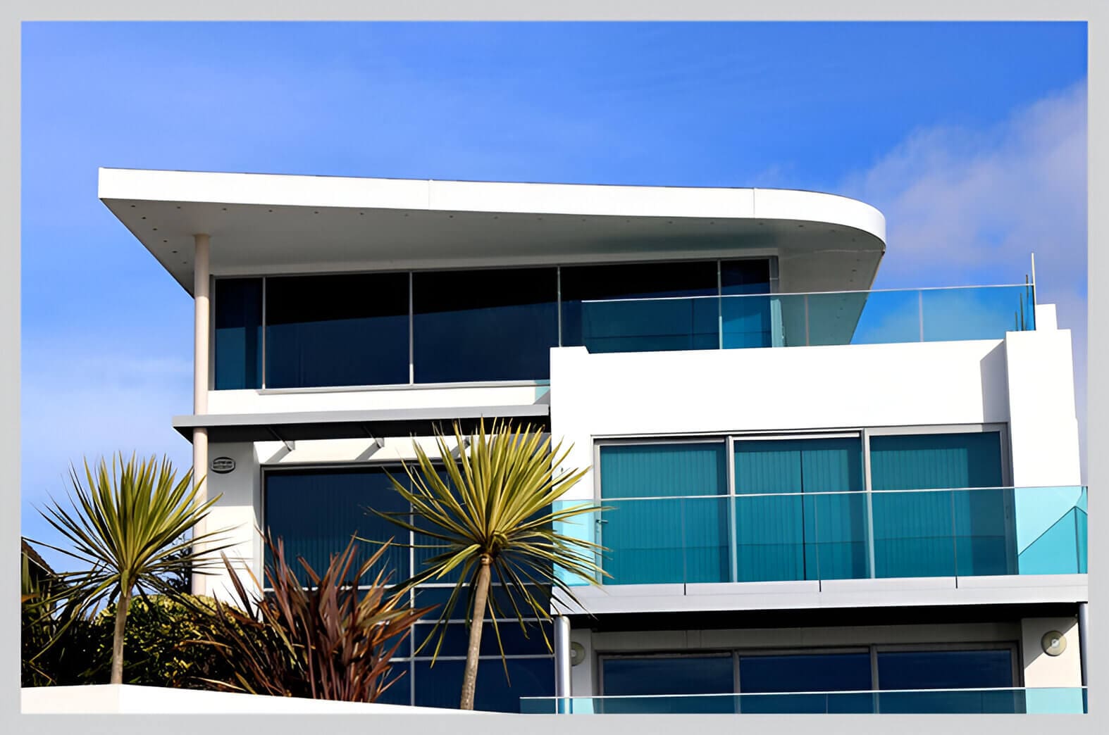 A large white building with glass windows and palm trees.